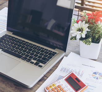 Reports and a calculator on a table next to a laptop